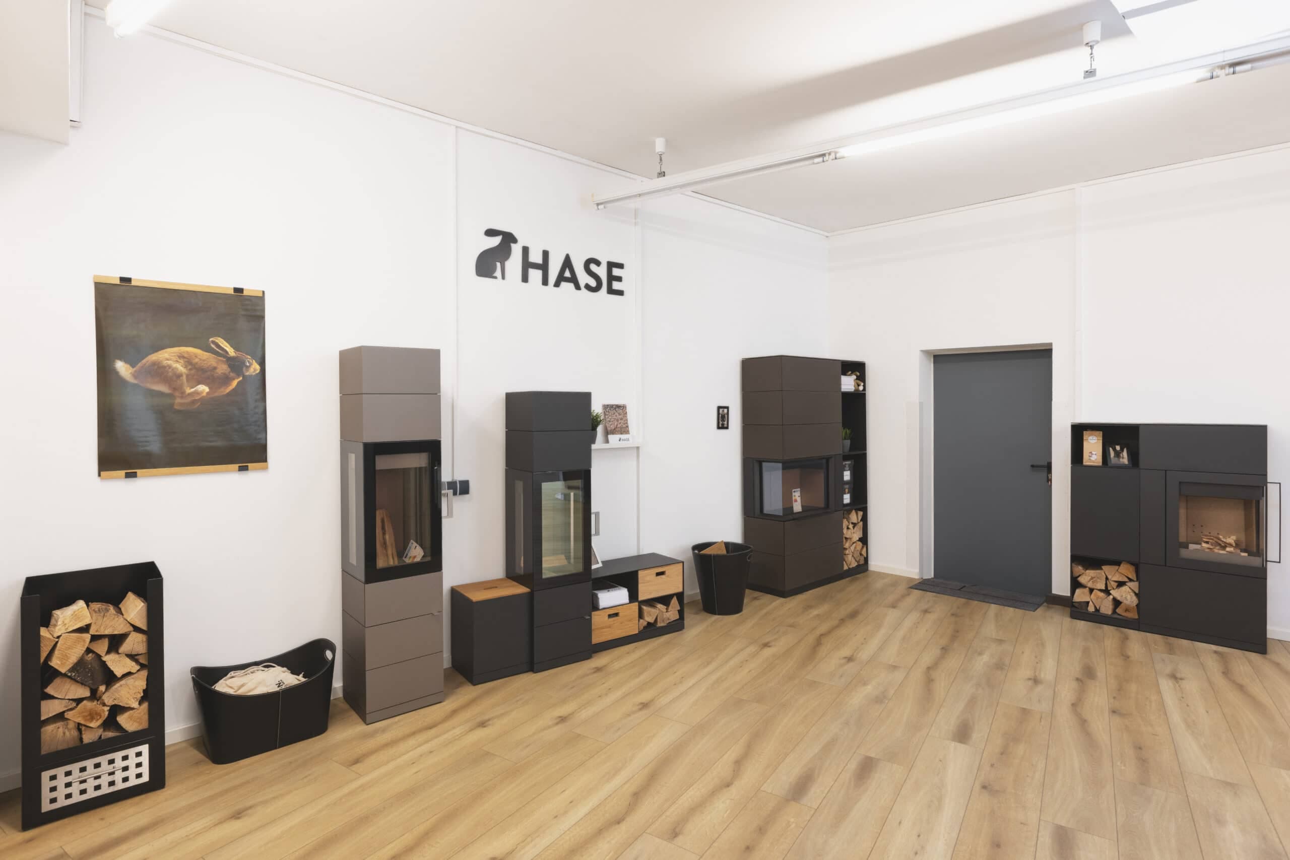 Ausstellungsraum mit mehreren Kaminöfen der Marke Hase in schwarzer und grauer Ausführung, teilweise mit Holzlagerung,