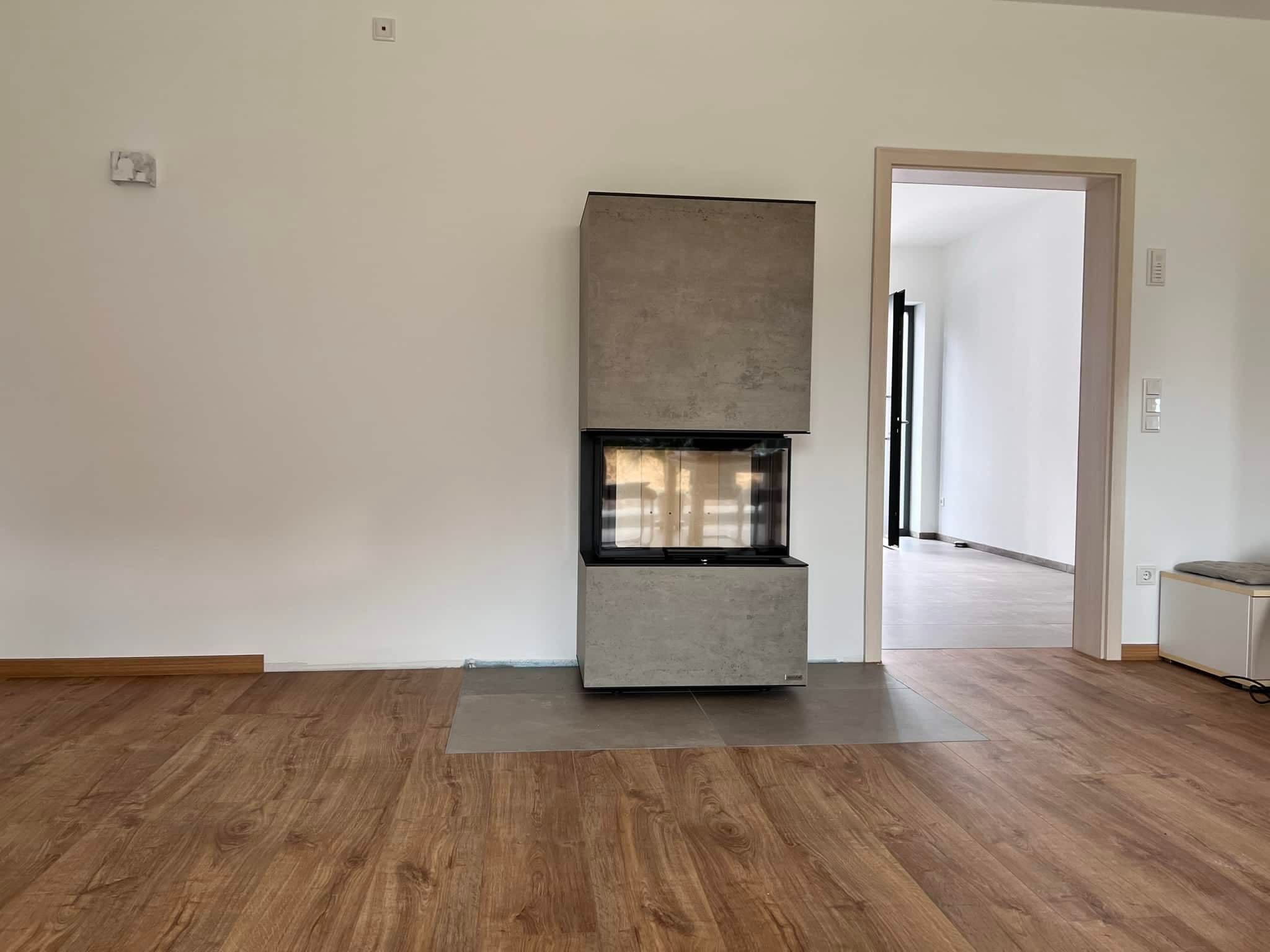 Kaminofen neocube P20 mit Betonverkleidung in Riverwashed-Optik und schwarzem Rahmen, ausgestellt in hellem Wohnraum mit