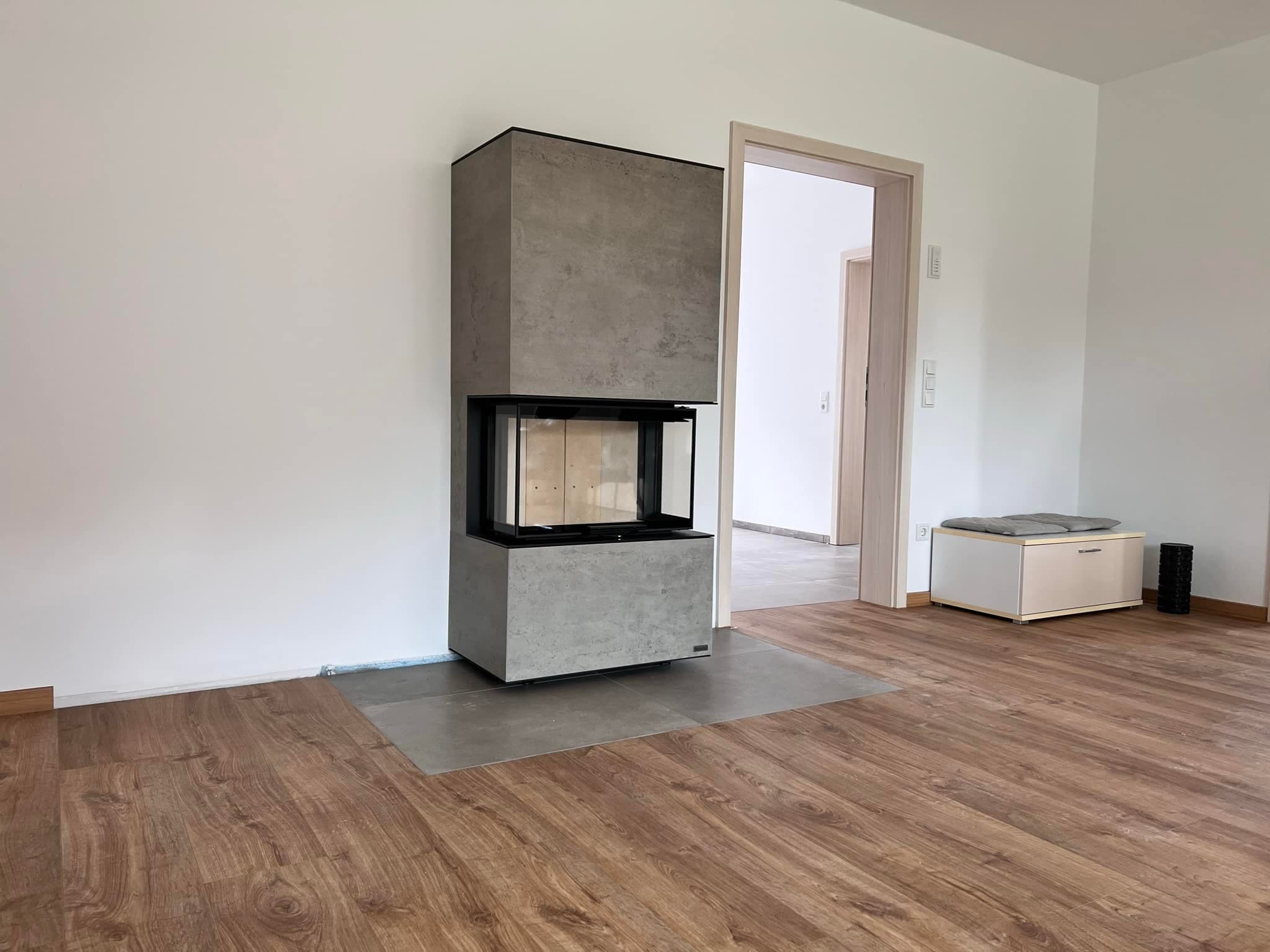 Moderner Speicherofen neocube P20 mit Betonoberfläche und schwarzer Glasscheibe in Ausstellungsraum mit Holzboden