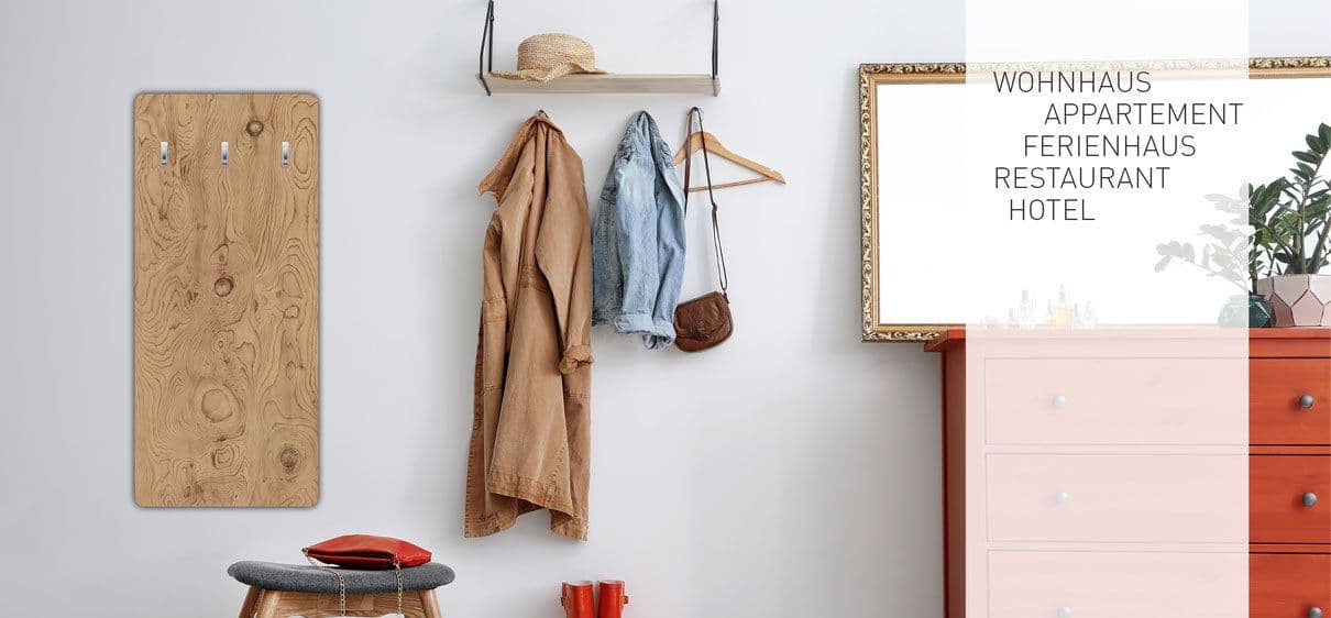 Helles Wohnzimmer mit Holz-Wandpaneel, Kleiderstange mit Jacken und Hut, grauem Polsterstuhl mit rotem Kissen, rosa Kommode