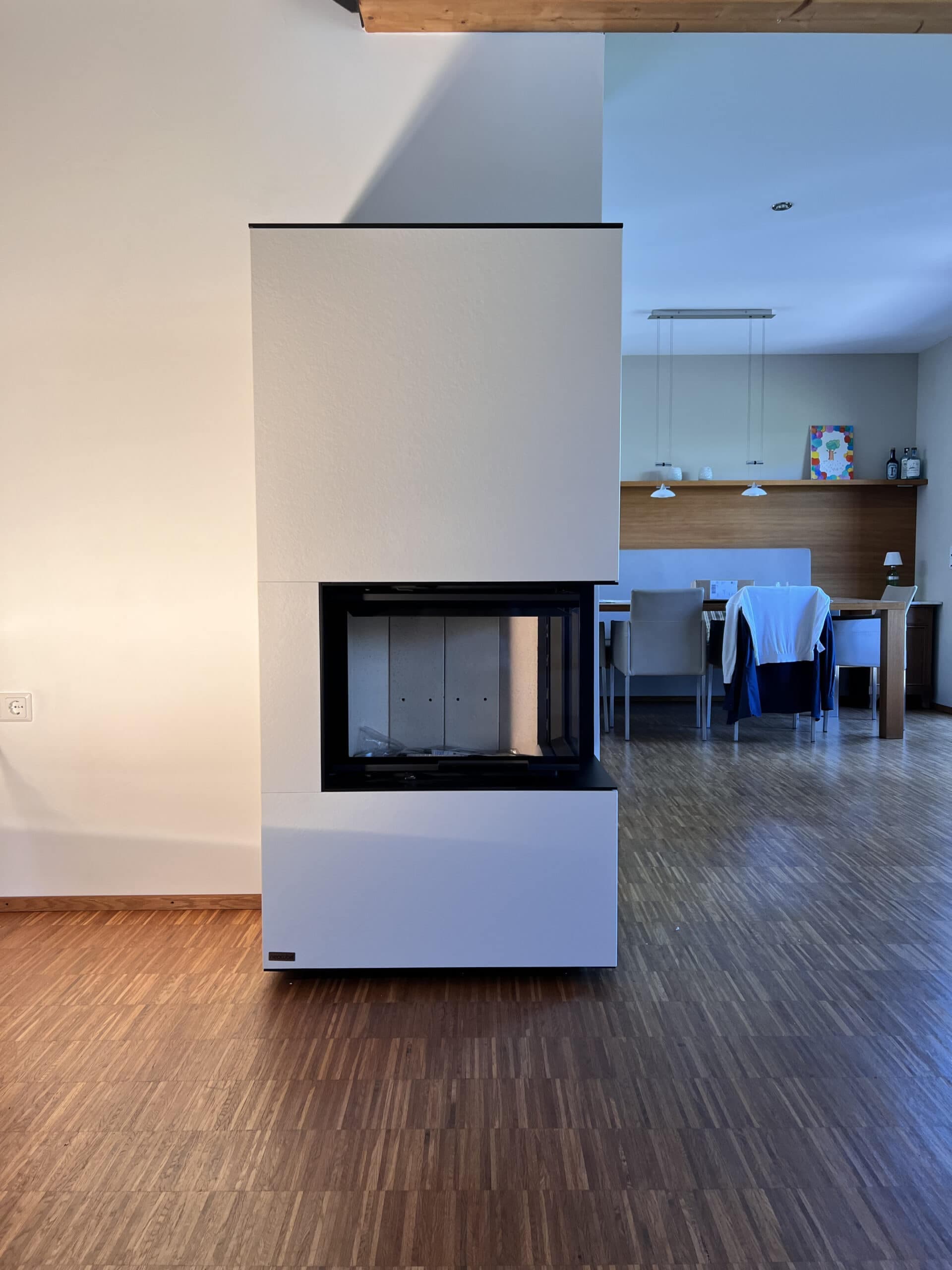 Moderner Speicherofen mit weißer Verkleidung und schwarzem Kamineinsatz in minimalistischem Wohnraum