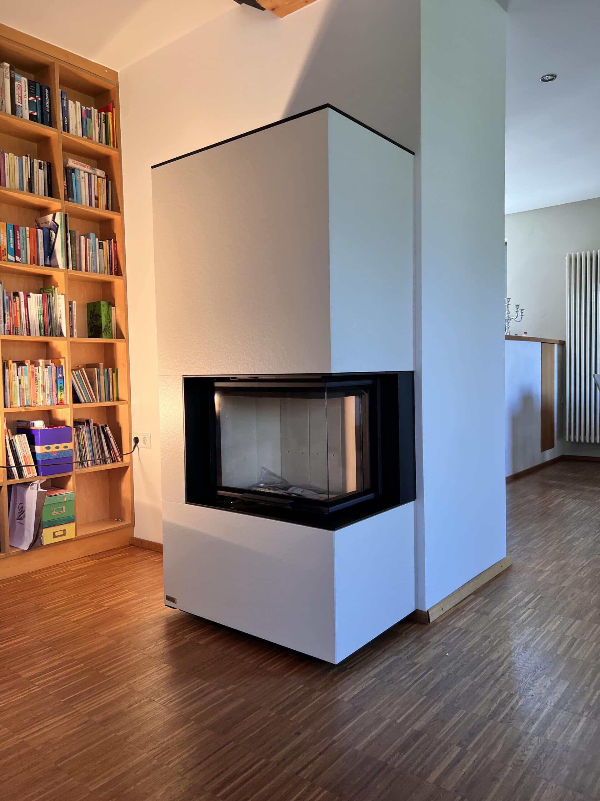 Kaminkassette mit schwarzem Stahlrahmen in weißer Pfeilerabdeckung, drei Seiten sichtbar, in modernem Wohnzimmer mit