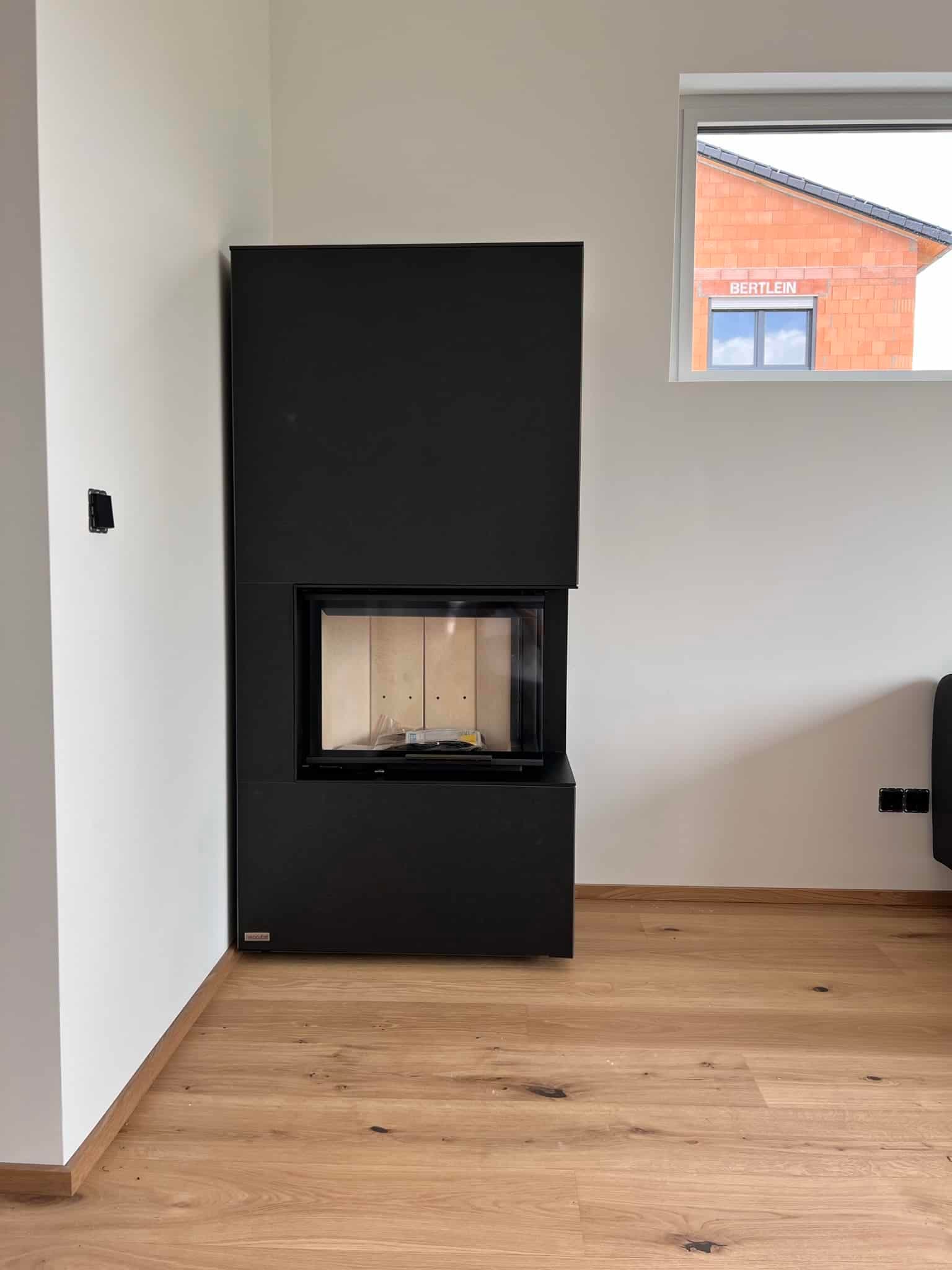 Kaminofen mit schwarzem Korpus und Glasfront in modernem Wohnraum, eingebaut in weiße Wand mit Holzboden