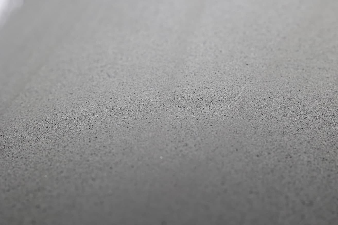 Detailaufnahme einer graubeigen Oberfläche mit feiner körneriger Textur und Lichtreflexen