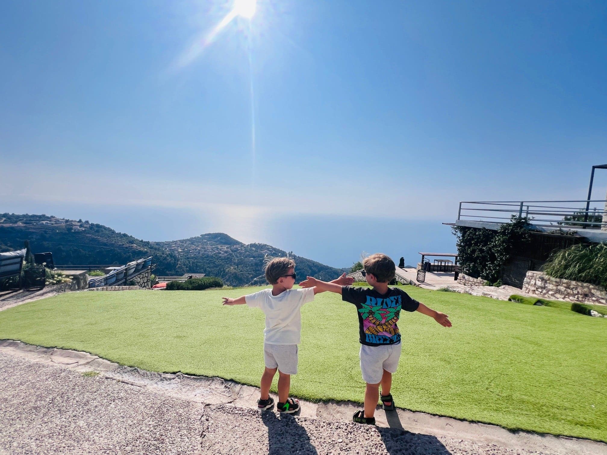 Zwei Kinder spielen auf einer grünen Wiese mit Meerblick auf eine hügelige Küstenlandschaft