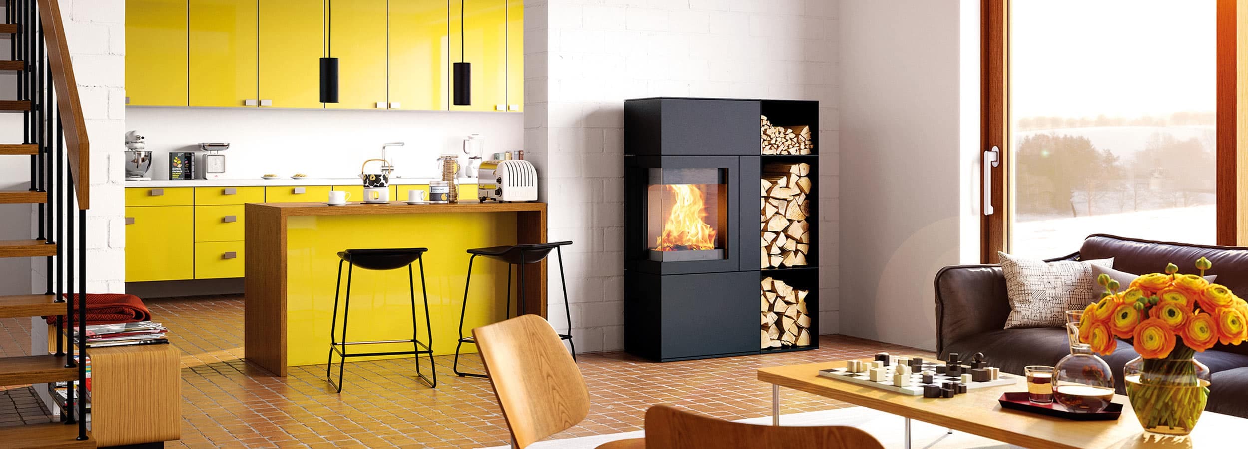 Schwarzer Kaminofen Hase Sendai Pro 135 mit brennendem Feuer und Holzlagerraum in modernem Wohnzimmer mit gelber Küche und