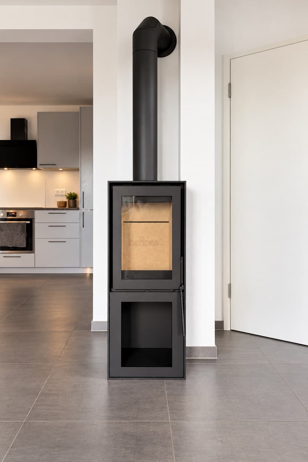 Barbas BOX 20/45 in Schwarz mit offenem Holzfach im Sockel, aufgestellt vor einem weißen Wandvorsprung in einem Wohnraum in Rimpar, dahinter die offene Küche.