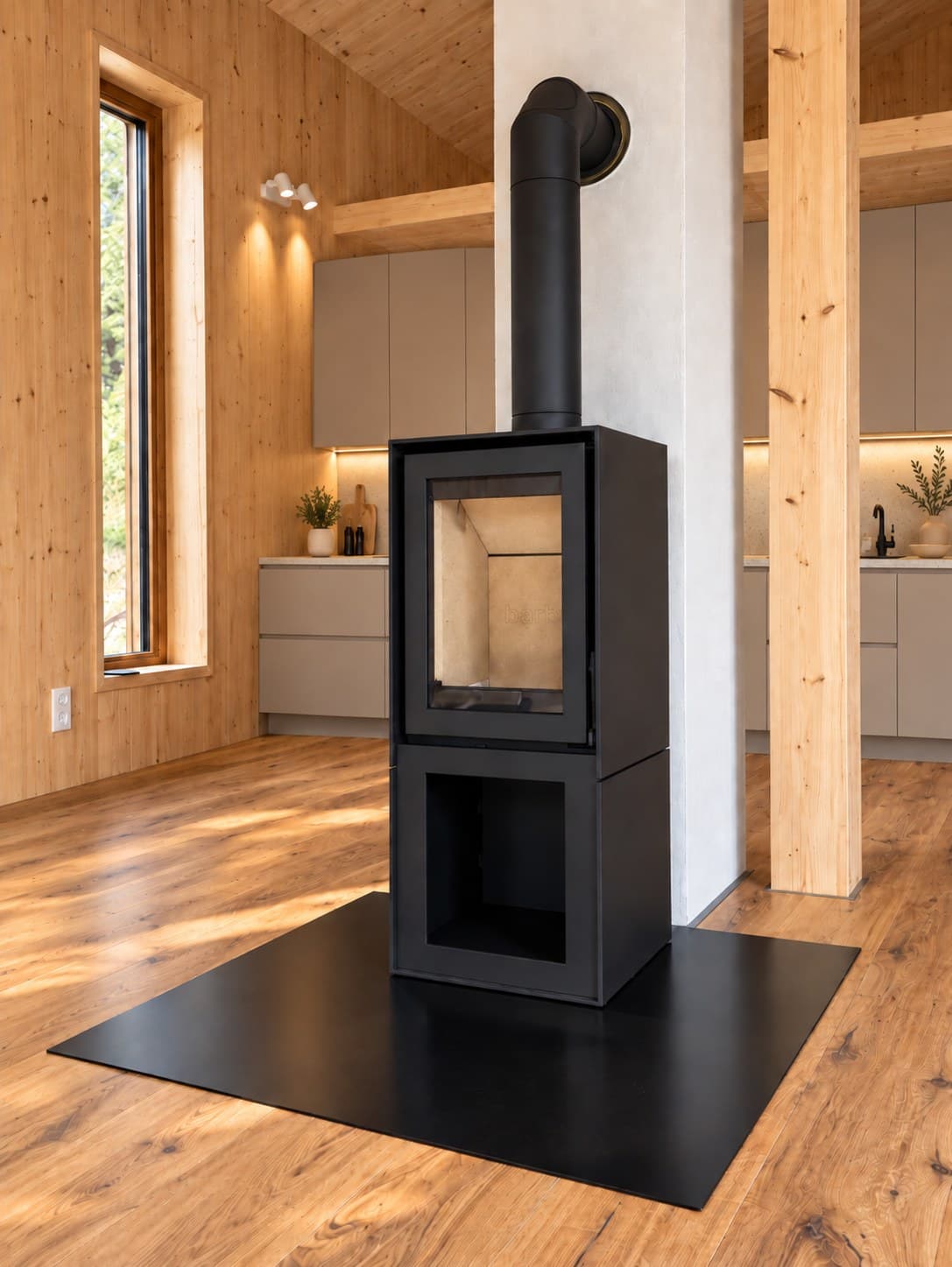 Barbas BOX 20/45 als freistehender Holzkamin mit schwarzem Stahlkorpus und offenem Holzfach im Sockel, aufgestellt auf einer schwarzen Bodenplatte in einem Wochenendhaus in der Rhön mit Wänden, Decke und Boden aus Holz.