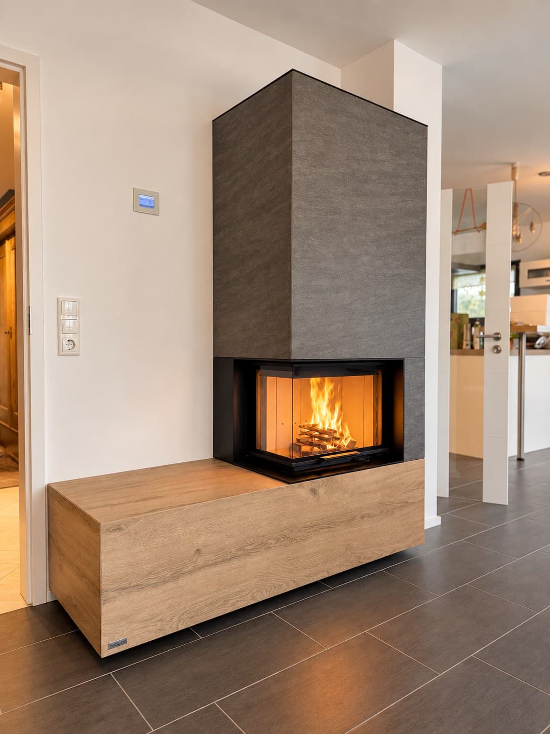 neocube C23 als Eckkamin in Bergtheim: Feuerraum über Eck verglast, darunter eine Bank in Eichenoptik, darüber die Verkleidung in dunkelgrauer Keramik.