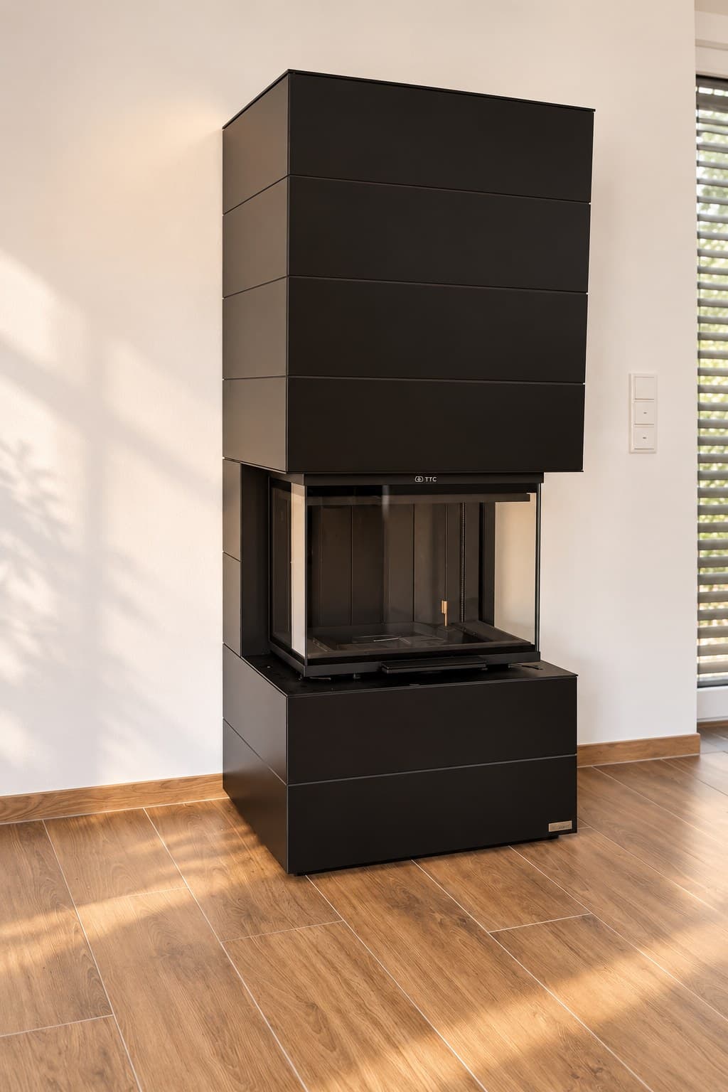 neocube P10 aus der black & white Edition in Schwarz, dreiseitig verglaster Kaminbausatz mit waagerecht gegliederter Sinterkeramik, freistehend vor einer weißen Wand auf Holzboden in Würzburg-Lengfeld.