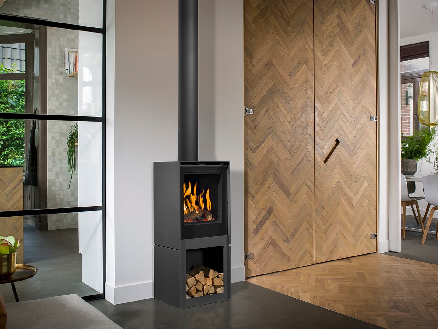 Schwarzer Gaskaminofen Barbas Box Gas 45 in modernem Wohnraum mit Holzherringbone-Verkleidung und Brennholzlager unten