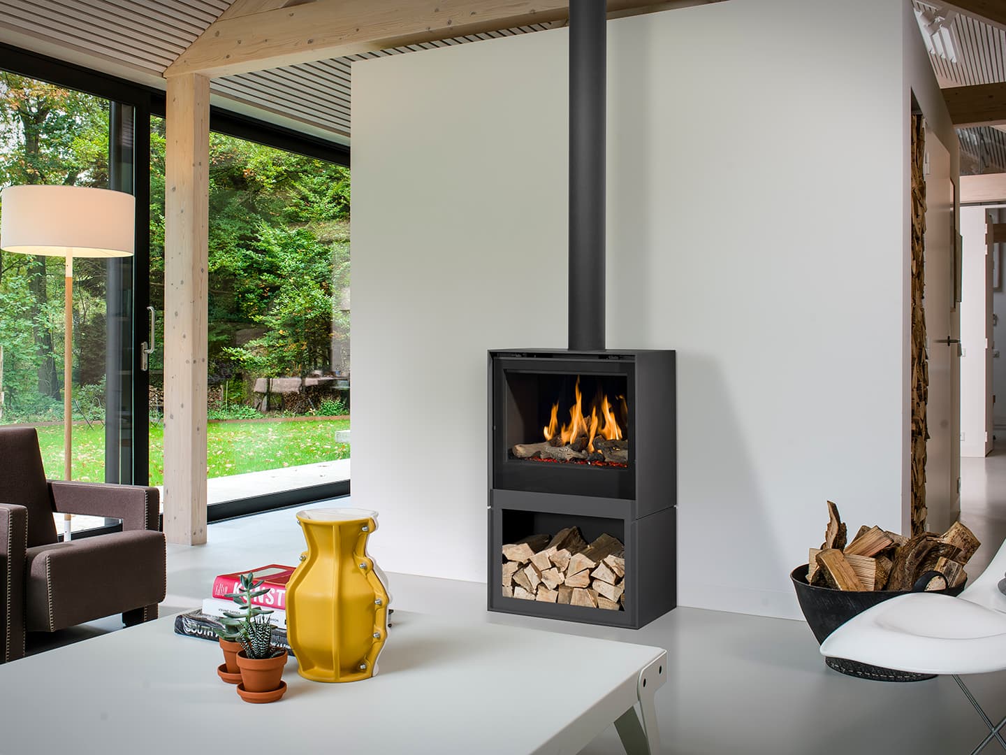 Schwarzer Gaskaminofen Barbas Box Gas 65 mit sichtbarer Flamme und Holzlager in modernem Wohnzimmer mit großer Glasfront zum