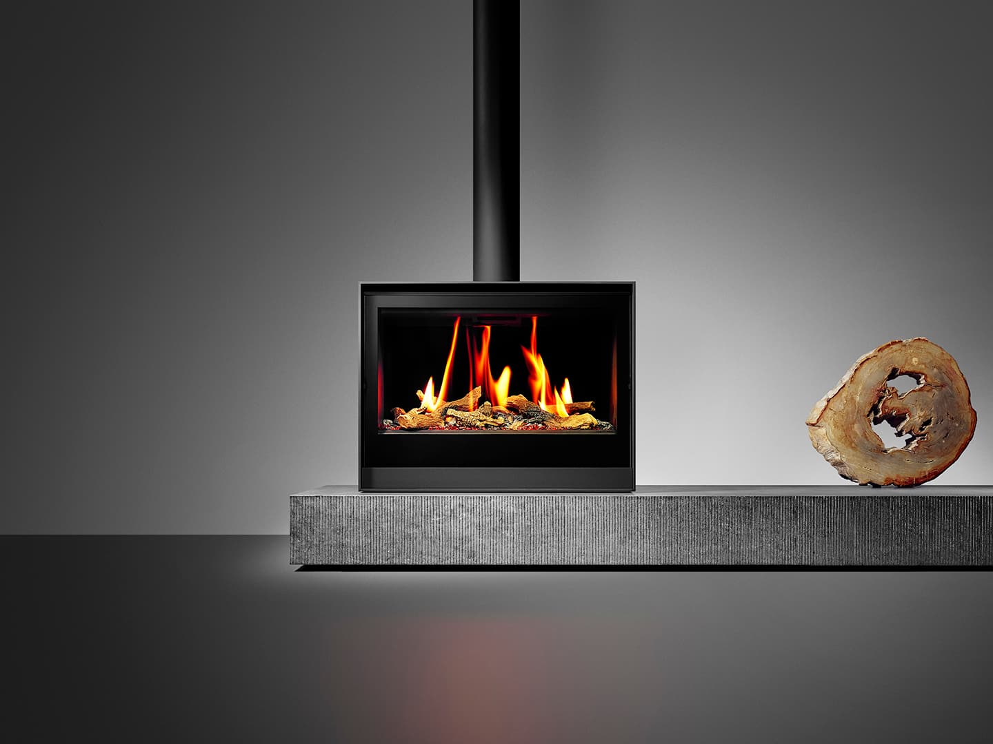 Gaskaminofen Barbas Box Gas 80 mit schwarzem Rahmen auf grauer Kaminverkleidung, brennendes Feuer mit Holzdekor sichtbar